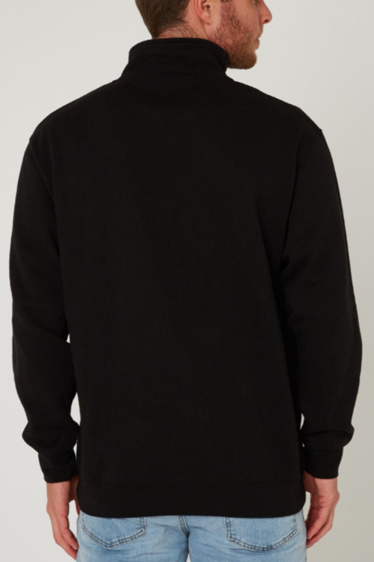 A man wearing a black Pilbara Classic Fleece Pullover and light blue jeans stands with his back to the camera, looking slightly to the right.