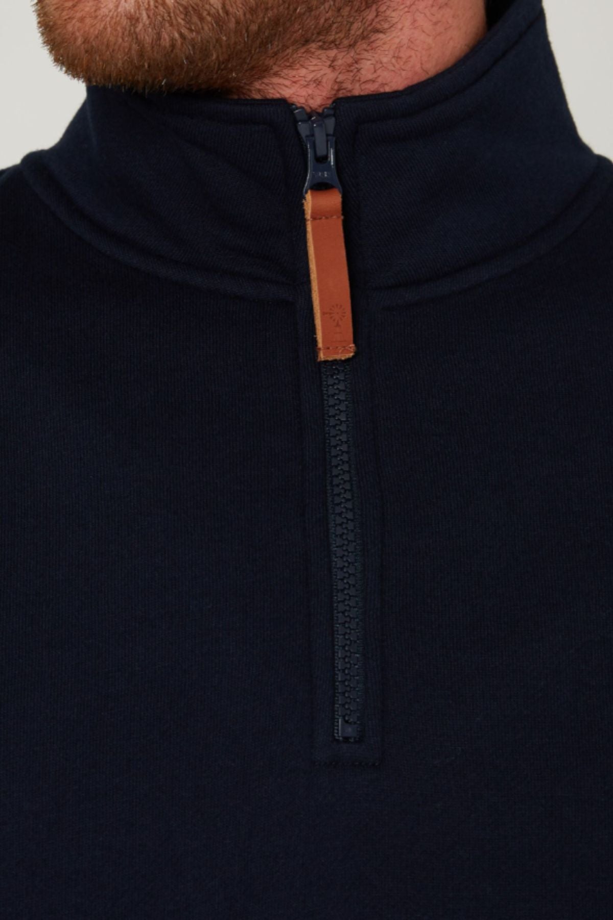 Close-up of a person wearing a navy blue Pilbara Classic Fleece Pullover, featuring a quarter-zip front with a brown leather pull tab; only the lower face and neck are visible.