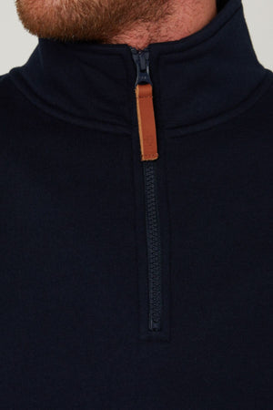 Close-up of a person wearing a navy blue Pilbara Classic Fleece Pullover, featuring a quarter-zip front with a brown leather pull tab; only the lower face and neck are visible.
