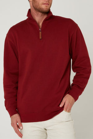 A man stands against a plain light background wearing a maroon Pilbara Classic Fleece Pullover with a high collar, paired with beige pants. His left hand is on his hip and his right hand rests by his side.