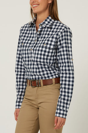 A woman smiles against a light background, wearing the Pilbara Ladies Check Closed Front Long Sleeve Shirt in navy and white, tucked into tan pants with a brown belt. Her long hair is down.