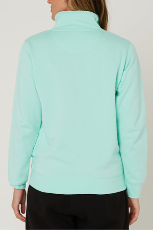 A person is seen from the back wearing the Pilbara Ladies Classic Fleece Pullover in light turquoise with black pants. The plain background highlights the pullover's cozy fleece lining and high-collar, long-sleeve design.
