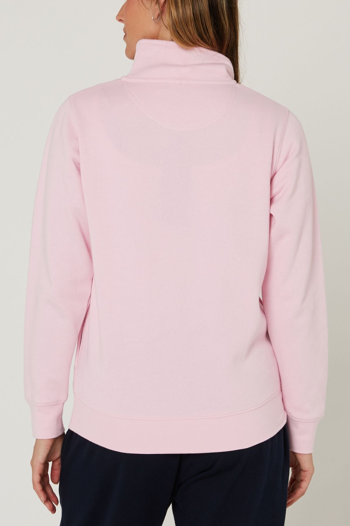 A person stands facing away, wearing the Pilbara Ladies Classic Fleece Pullover in light pink with dark pants against a plain, light-colored background.