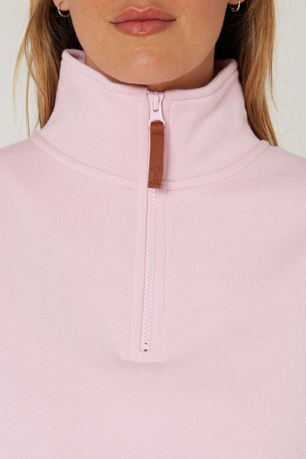 A close-up of a woman wearing a light pink Pilbara Ladies Classic Fleece Pullover, featuring fleece lining and a brown leather zipper pull; only her lower face, neck, and upper chest are shown.