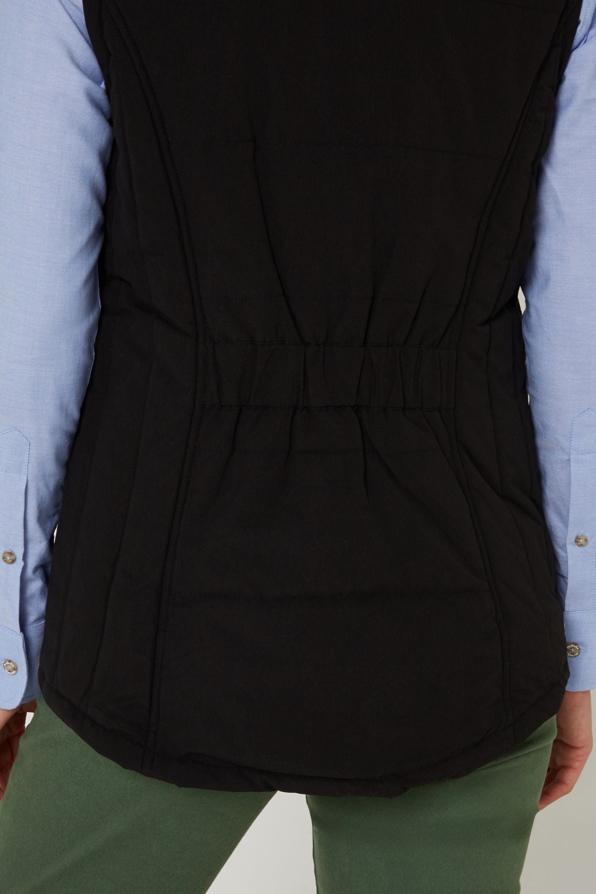 A person viewed from the back wears a light blue long-sleeve shirt, green pants, and the Pilbara Ladies Vest—a black winter vest with polyfill padding and an elastic waistband.