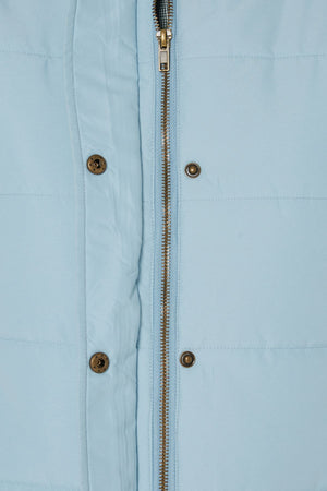 Close-up of the Pilbara Ladies Vest in light blue, showcasing quilted texture, polyfill padding, a zipper closure, and metallic snap buttons along the front placket. The detailed stitching and fabric texture are clearly visible.