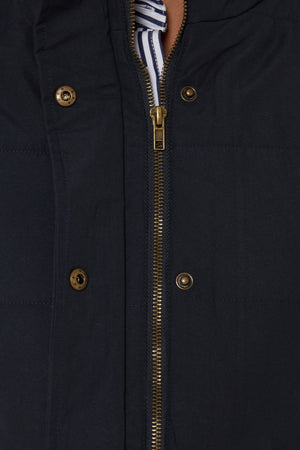 Close-up of the Pilbara Ladies Vest, a dark microfiber waterproof vest with gold zipper and buttons. Partially unzipped to reveal its polyfill padding and a blue-and-white striped garment underneath.