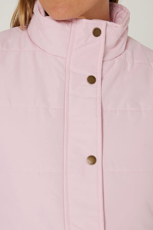 Close-up of a person wearing the Pilbara Ladies Vest—a light pink quilted vest with Polyfill padding, high collar, and metal snap buttons. The lower part of the face is partially shown.