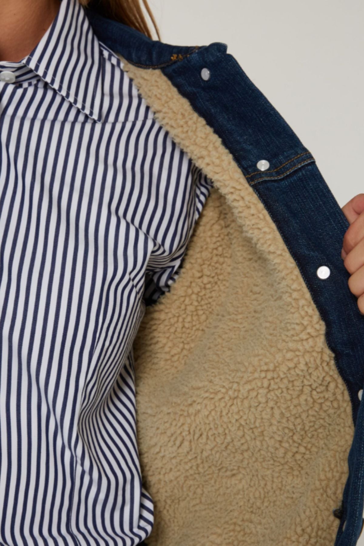 A person in a blue and white striped shirt holds open the Pilbara Lauren Sherpa Lined Jacket, showing its beige fleece lining.