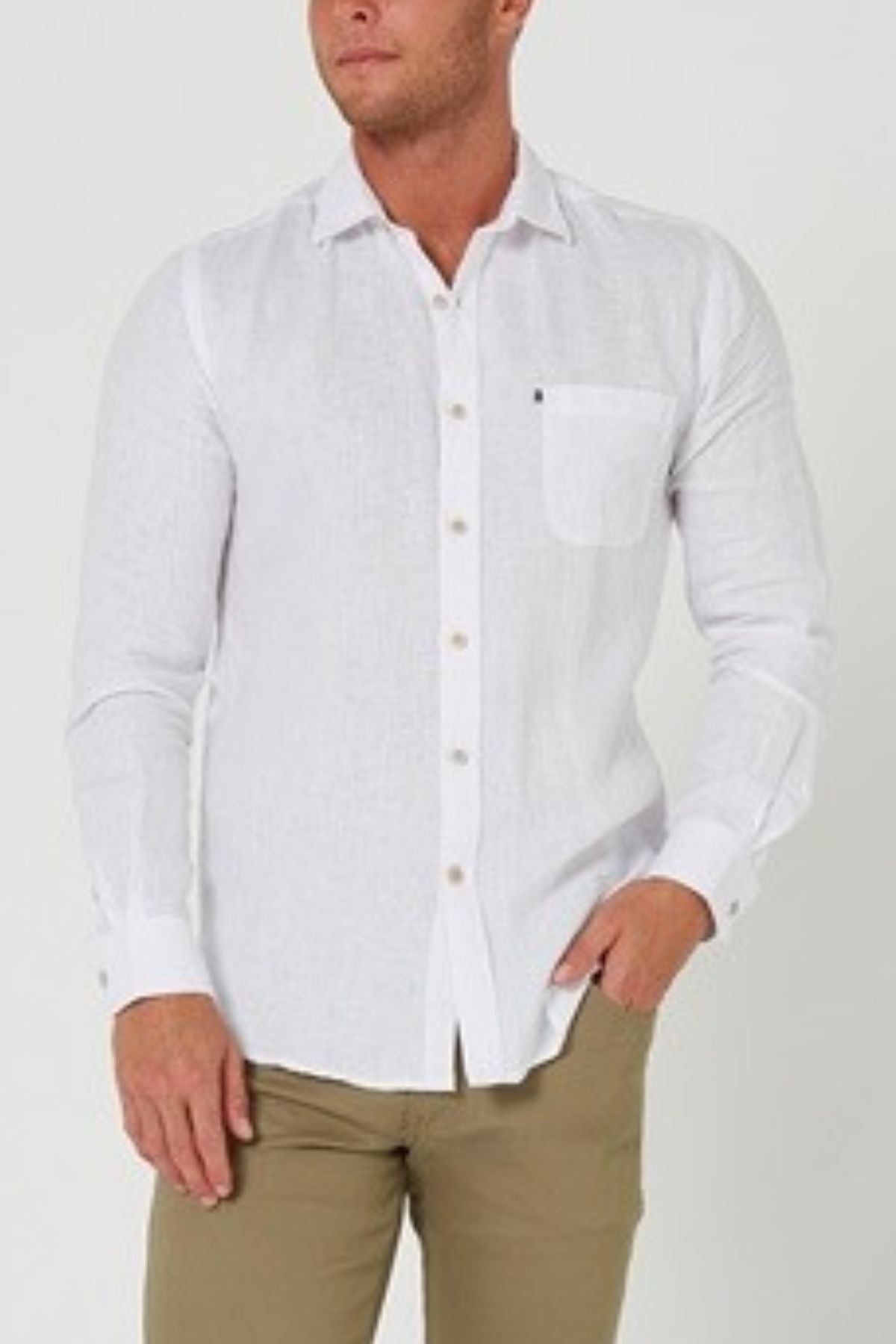 A man models the Pilbara Linen Shirt—long-sleeve, white, 100% linen—with khaki pants against a light background. His left hand is in his pocket while his right hand rests at his side, highlighting classic style.