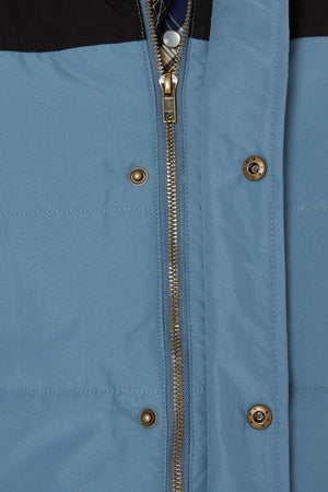Close-up of the Pilbara Two Tone Vest with polyfill padding, brass zipper, and metallic snap buttons. This blue waterproof vest features a black upper section and detailed stitching.