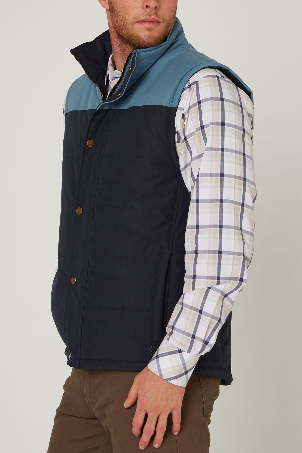 A man wears the Pilbara Two Tone Vest with polyfill padding over a white and blue plaid shirt and brown pants, standing with one hand in his pocket, facing slightly to the side.