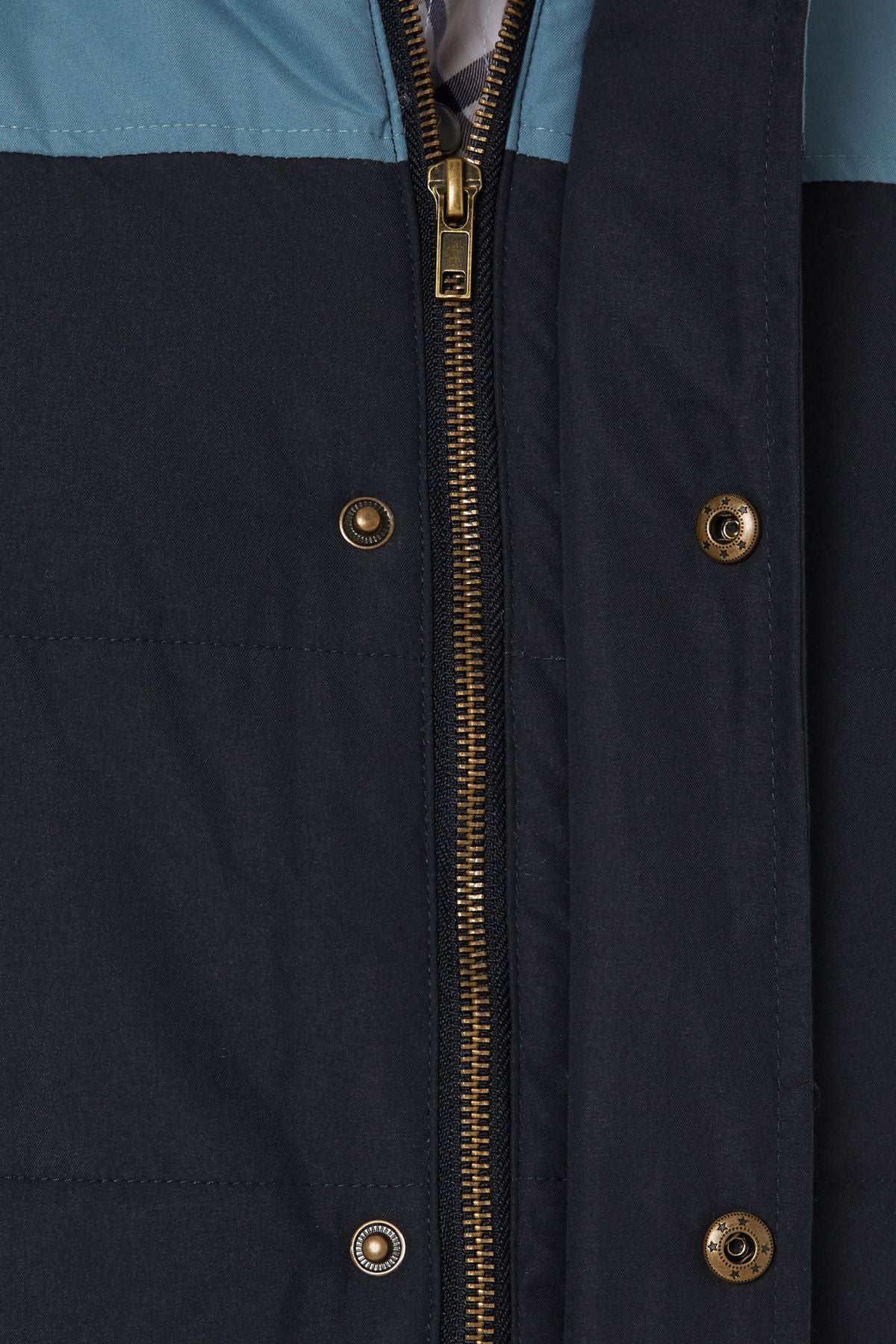 Close-up of the Pilbara Two Tone Vest, featuring a brass zipper, snap buttons, visible stitching, and cozy polyfill padding. The vest is mainly dark blue with a lighter blue top section for added style and warmth.