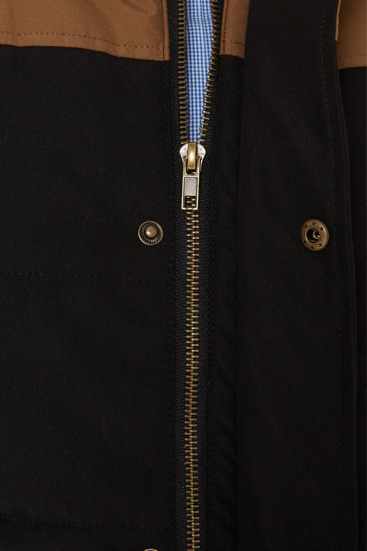 Close-up of the Pilbara Two Tone Vest, featuring a classic fit, metal zipper, brown and black color block design, blue and white checkered shirt fabric behind the zipper, and two metallic snap buttons on the black section.