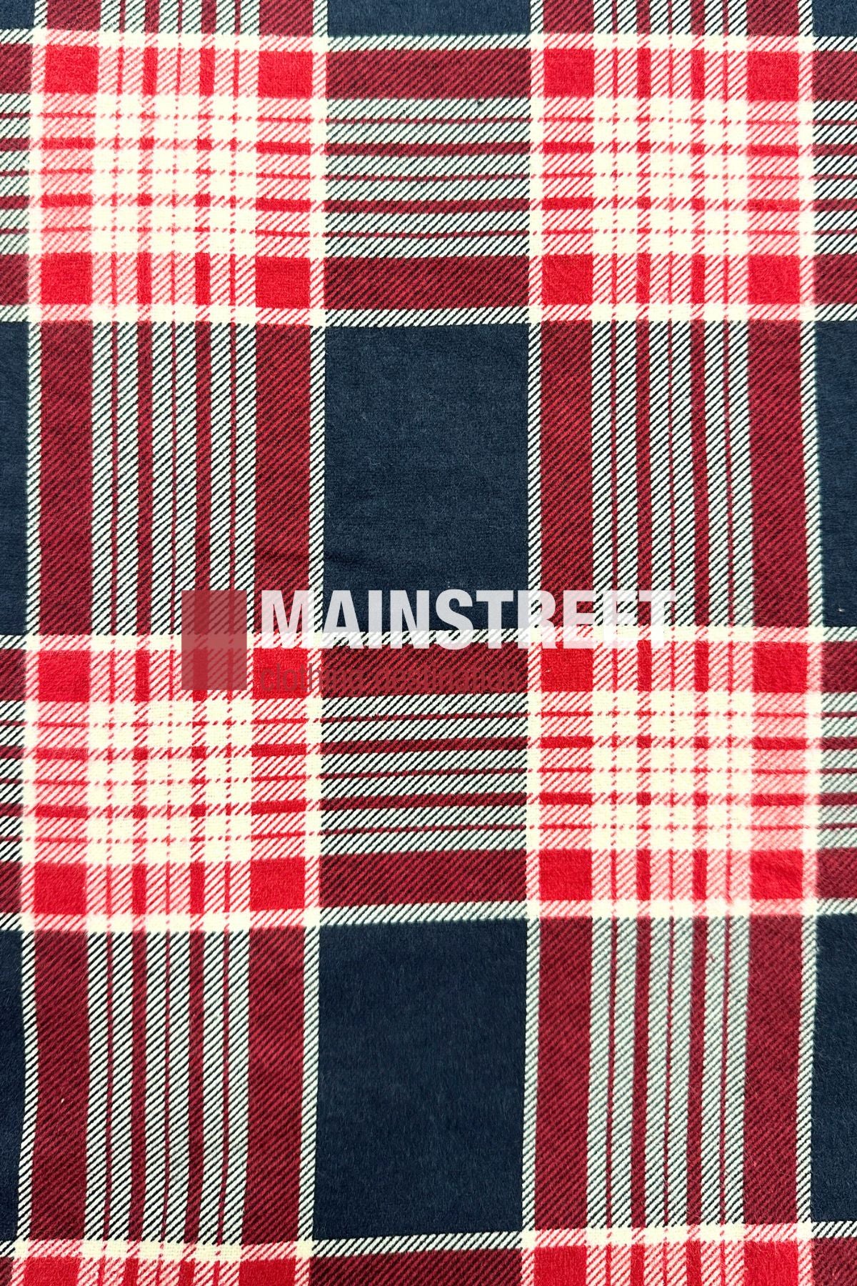The Pilgrim Closed Front Flannelette Shirt features a red, white, and navy blue large plaid pattern with intersecting lines. Made from 100% cotton, it has long sleeves and "MAINSTREET" printed boldly in white across the center.