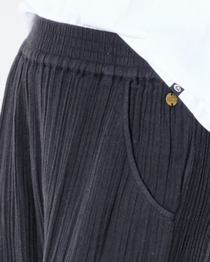 A person wears Rip Curl Premium Surf Beach Pants featuring a dark pleated design, smocked waist, and elastic waistband. A small metal tag near the pocket complements the casual beach vibe, while the hem of a white shirt peeks out above the waistband for a relaxed style.