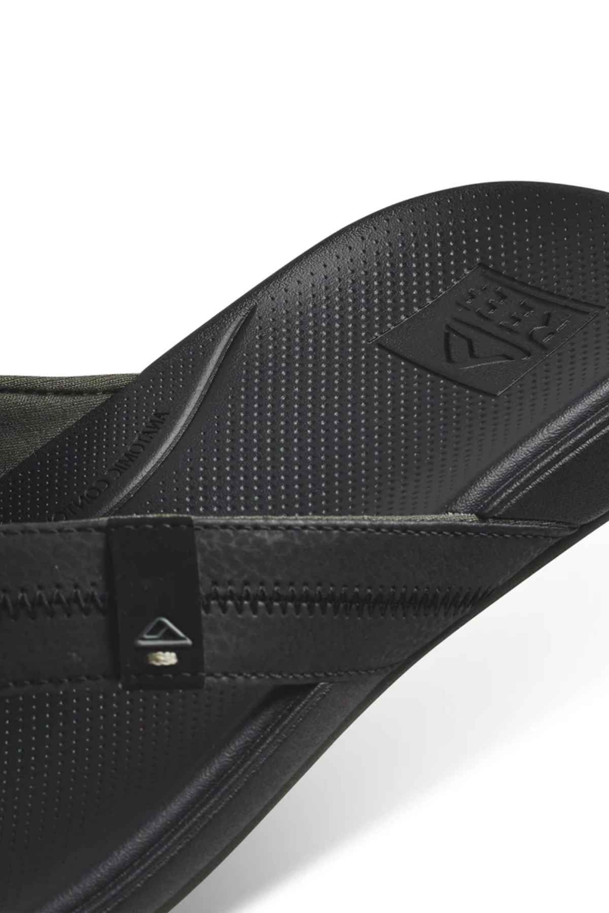 Close-up of a black REEF Cushion Phantom 2.0 flip-flop, highlighting its textured footbed, branded strap and sole, durable synthetic material with subtle stitching, and design focused on all-day comfort and arch support.