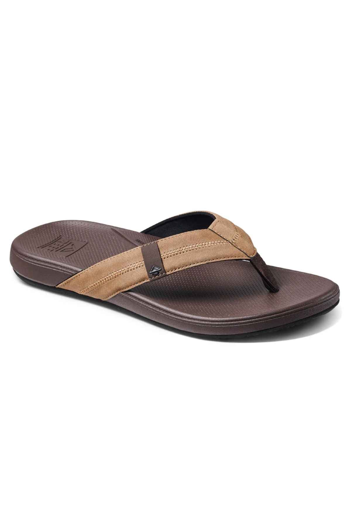 The REEF Cushion Phantom 2.0 is a brown flip-flop sandal featuring a textured sole, two-tone dark brown and tan strap, and a molded rubber outsole for durability, shown on a white background.