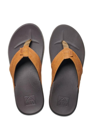 A pair of REEF Cushion Phantom LE thong flip-flops in brown and black with full grain leather straps and textured soles, shown from above on a white background.