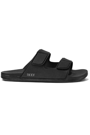 The REEF Cushion Tradewind sandal in black features two wide adjustable straps, a cushioned footbed, and the subtle "REEF" logo on the side of the sole.