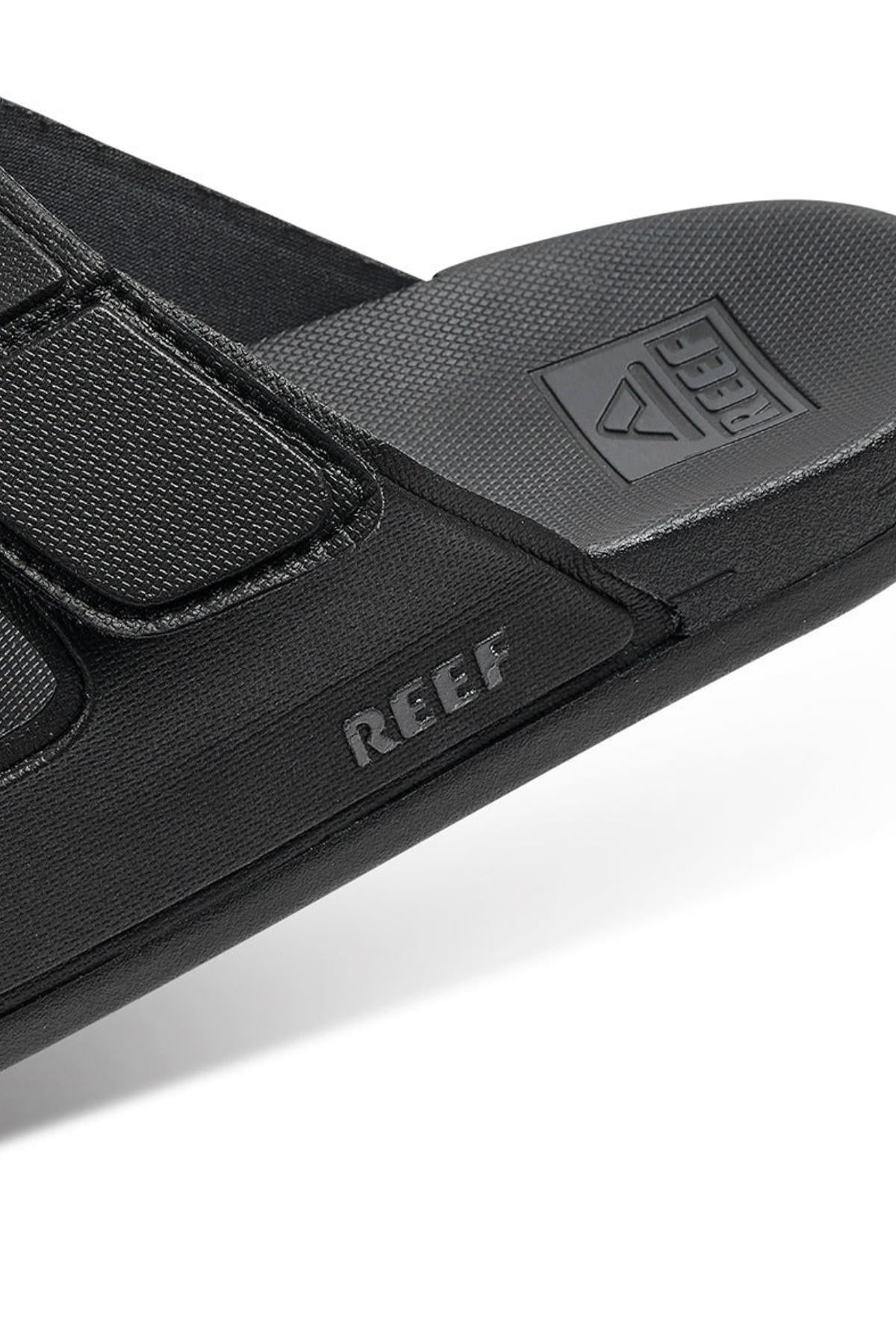 Close-up of the black REEF Cushion Tradewind sandal featuring a textured strap, "REEF" branding on the side, and logo on the cushioned footbed. The sandal offers a casual, sporty look.