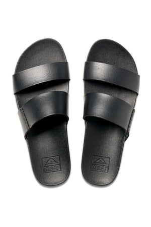 The REEF Cushion Vista sandals are designed with two wide, black vegan leather straps across the top. They feature an embossed brand logo near the heel on the footbed and come equipped with a cushion bounce midsole for enhanced comfort. These simple yet stylish sandals are perfect for casual wear.