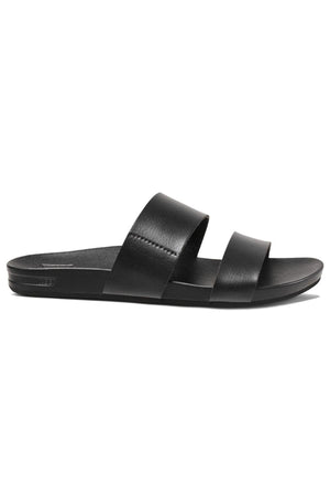 The REEF Cushion Vista is a black slide sandal with two wide vegan leather straps across the top and a flat sole, designed for casual wear. Featuring a cushion bounce midsole, this minimalist sandal is perfect for both indoor and outdoor use.