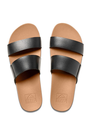 The REEF Cushion Vista is a pair of chic brown sandals featuring two wide black straps positioned parallel to each other over the top near the front and middle. The tan footbed includes a cushion bounce midsole, and the brand name "Reef" is embossed on the heel area.