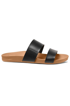 A side view of the REEF Cushion Vista sandal showcasing its stylish design with a tan footbed and sole, complemented by two wide, black leather straps crossing over the foot. This flat-soled sandal features a cushion bounce midsole for added comfort, making it both simple and casual.