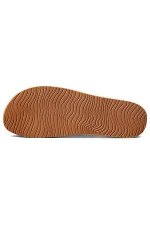 The image shows the sole of the REEF Cushion Vista sandal. The light brown sole, crafted from an EVA foam compound, features a wavy groove pattern designed to provide grip and traction. The sole appears flat and uniform, extending the length of the shoe for added comfort.