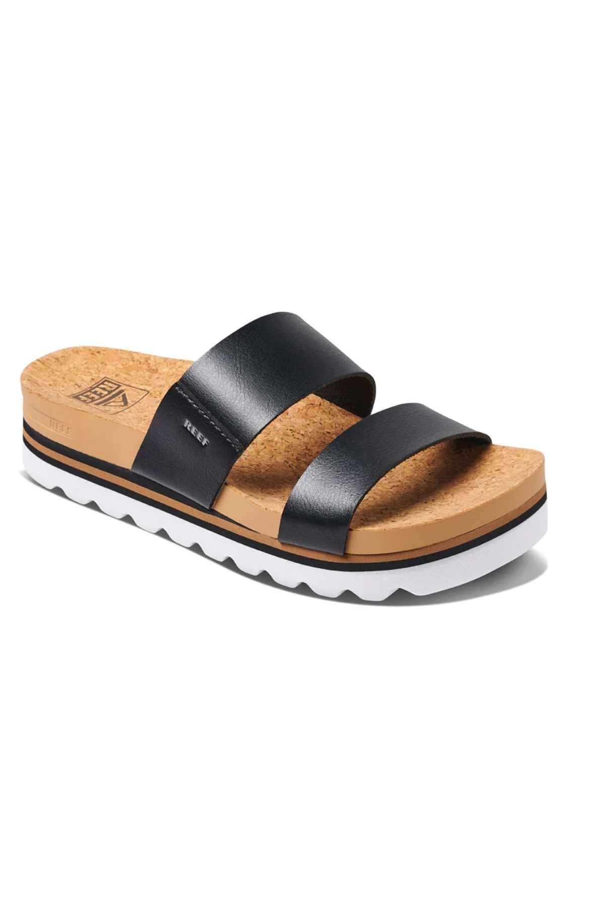 The REEF Cushion Vista Hi is a black sandal with two wide leather straps, a cushioned midsole for comfort, and a white and black zigzag-patterned sole for arch support. It has an angled design to showcase both side and top views over a cork insole.