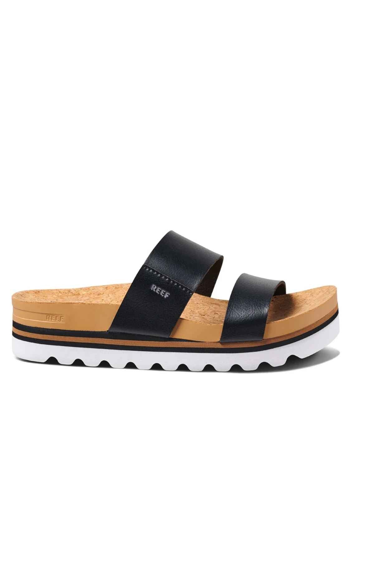 The REEF Cushion Vista Hi sandal features a tan cork footbed, dual black leather straps, a white sole with black accents, and wavy edge patterns. It includes a cushioned midsole for enhanced arch support.