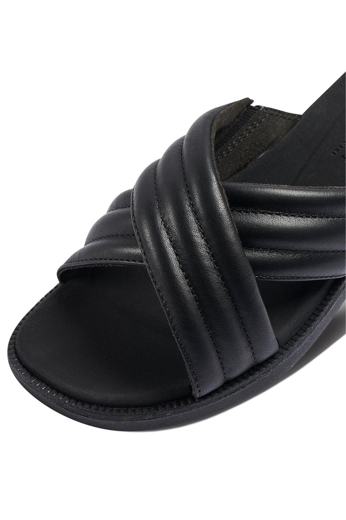 Close-up of the REEF Lofty Lux X, a black sandal with padded crisscross leather straps and a flat sole for premium comfort.