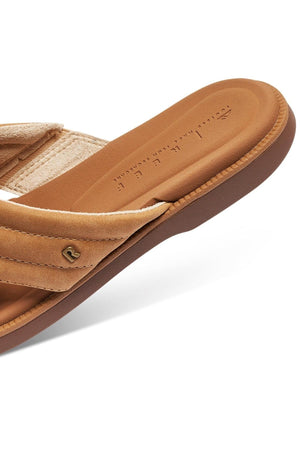 Close-up of the REEF Lofty Lux X tan slide sandal highlights its cushioned sole for premium comfort, soft fabric strap, small side metallic logo, and stamped text on the insole against a white background.