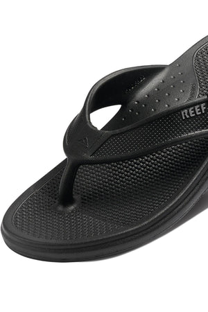 Close-up of a single black REEF Oasis flip-flop with a textured footbed and thong strap. The brand name "REEF" is visible on the side strap, and the design features arch support for added comfort. Made with renewable sugarcane EVA, these flip-flops are both stylish and sustainable.