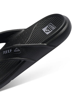 A close-up view of the black REEF Oasis sandal highlights its textured footbed and strap. The white letters of the Reef logo are clearly visible on the strap, while the brand's name is subtly etched into the footbed. Made with renewable sugarcane EVA and offering arch support, this sandal boasts a minimalist yet sporty design.