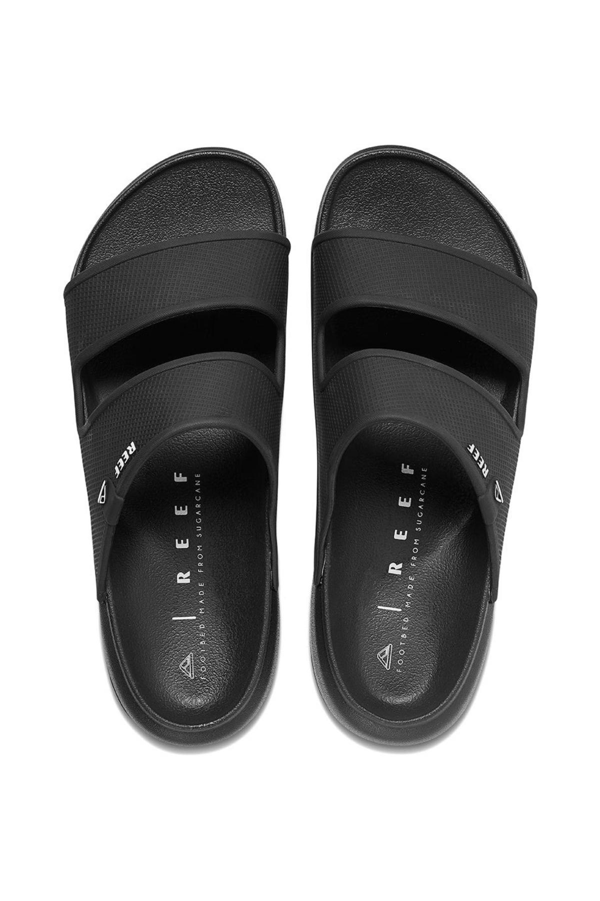 The REEF Oasis Double Up sandals are black slip-ons with dual wide foot straps, featuring "REEF" on the top strap. They offer a Cushion Lux insole with excellent arch support and are water-friendly, ensuring a sleek and stylish look when aligned side by side.