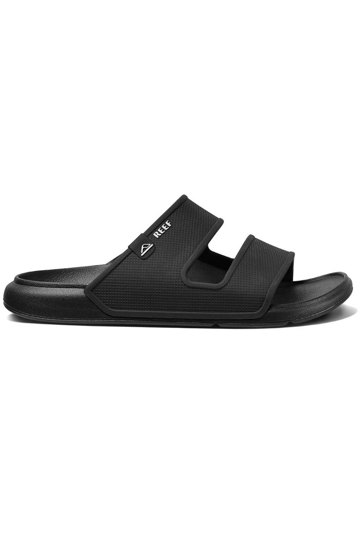 The REEF Oasis Double Up is a black slide sandal featuring two wide straps, a subtle logo, and a contoured footbed with arch support. It is water-friendly, has a textured sole for grip, and is designed for casual comfort.