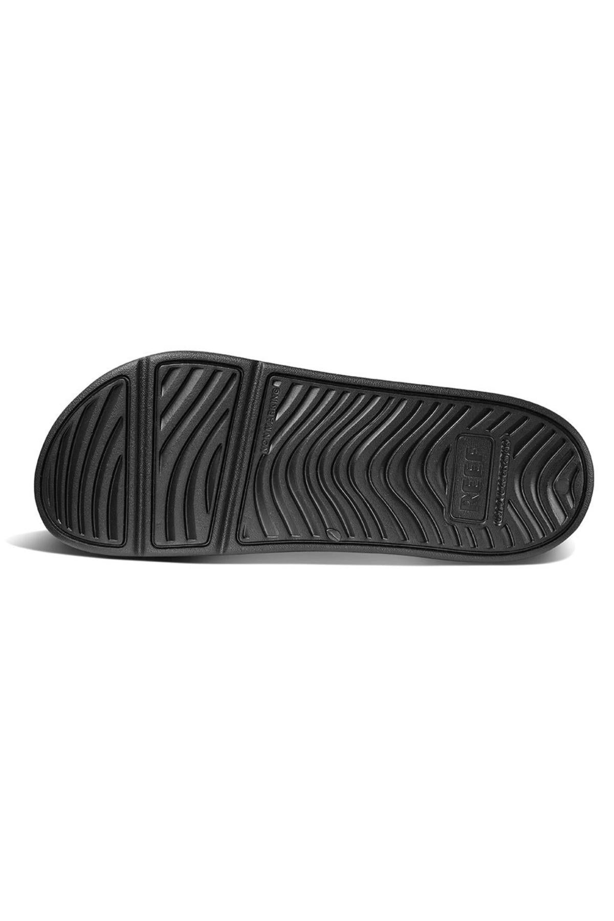 The image features the sole of a REEF Oasis Double Up sandal with a black wavy tread pattern, rectangular sections, and textured surface for grip. "Adidas" is embossed near the heel on one section.