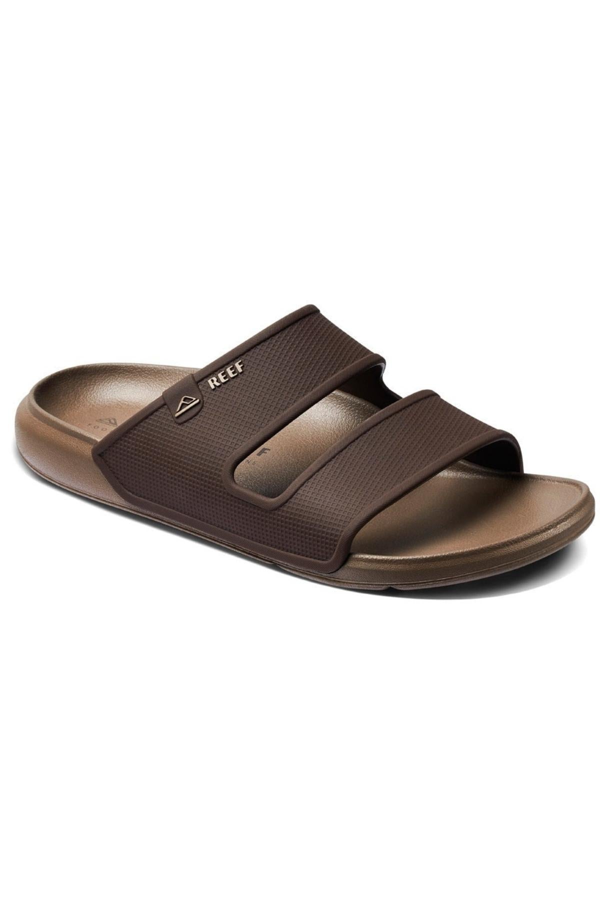 The REEF Oasis Double Up is a brown slide sandal with two adjustable straps, a molded sugarcane EVA footbed for arch support, and the Reef logo on the upper strap.