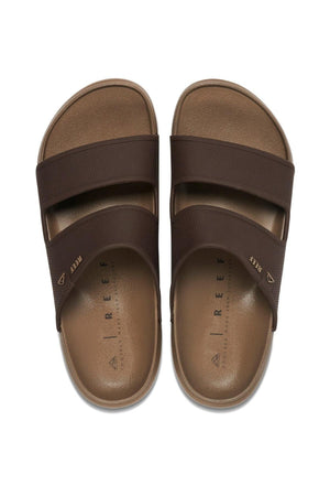 A pair of REEF Oasis Double Up slide sandals, brown with two wide straps per foot, shown from above on a white background. The tan footbeds offer arch support and are branded "REEF" inside each sandal.