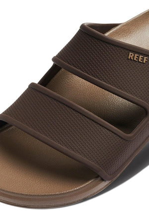Close-up of the REEF Oasis Double Up sandal with two wide textured straps, "REEF" embossed on the upper strap, and a smooth sugarcane EVA footbed with arch support in an open toe design.