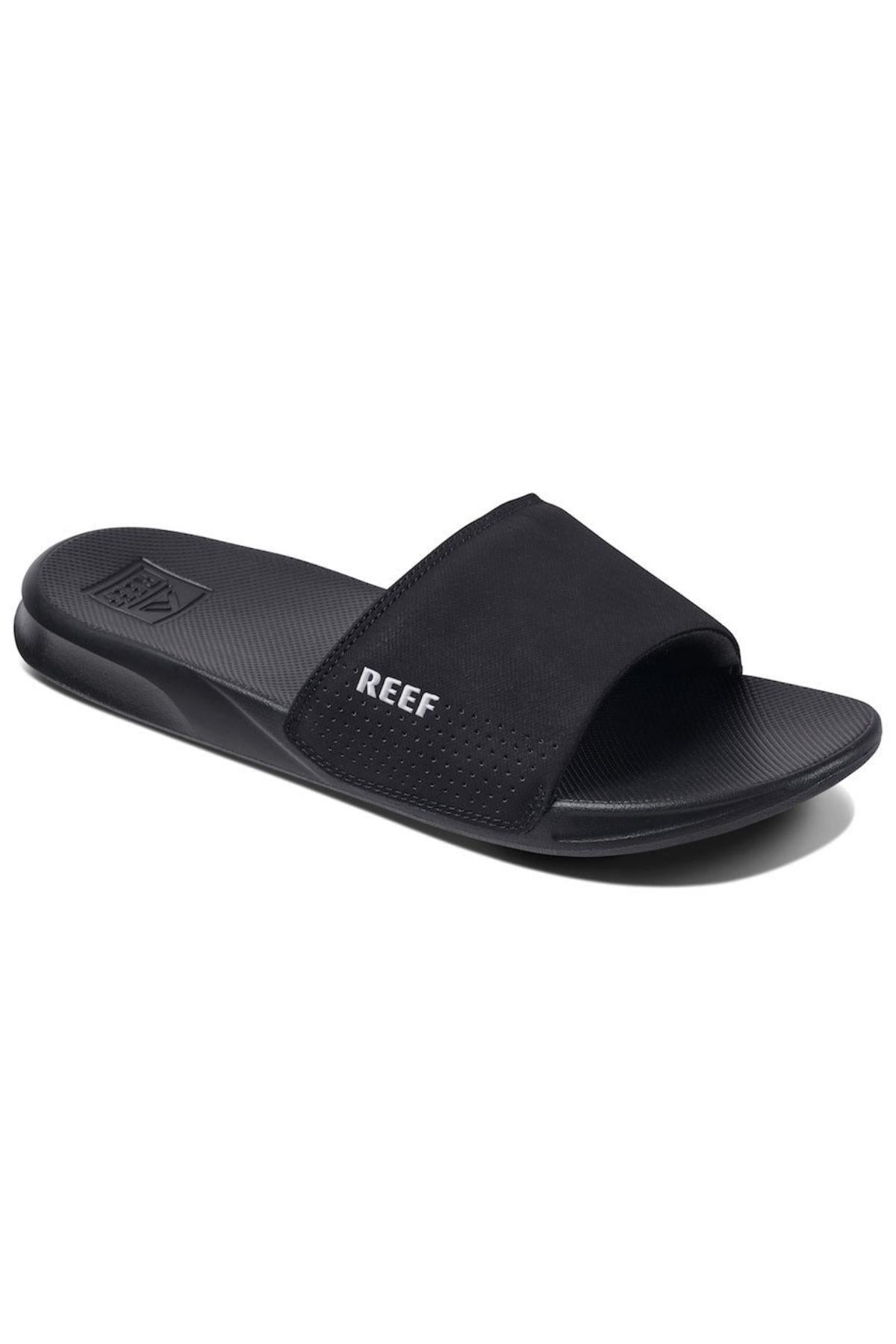 The REEF One Slide sandals feature a black design with an open toe, a wide strap across the midfoot adorned with the brand name "REEF" in white letters on the side, and a textured footbed. These stylish slides include a slightly contoured sole for added comfort, making them perfect for any casual outing.