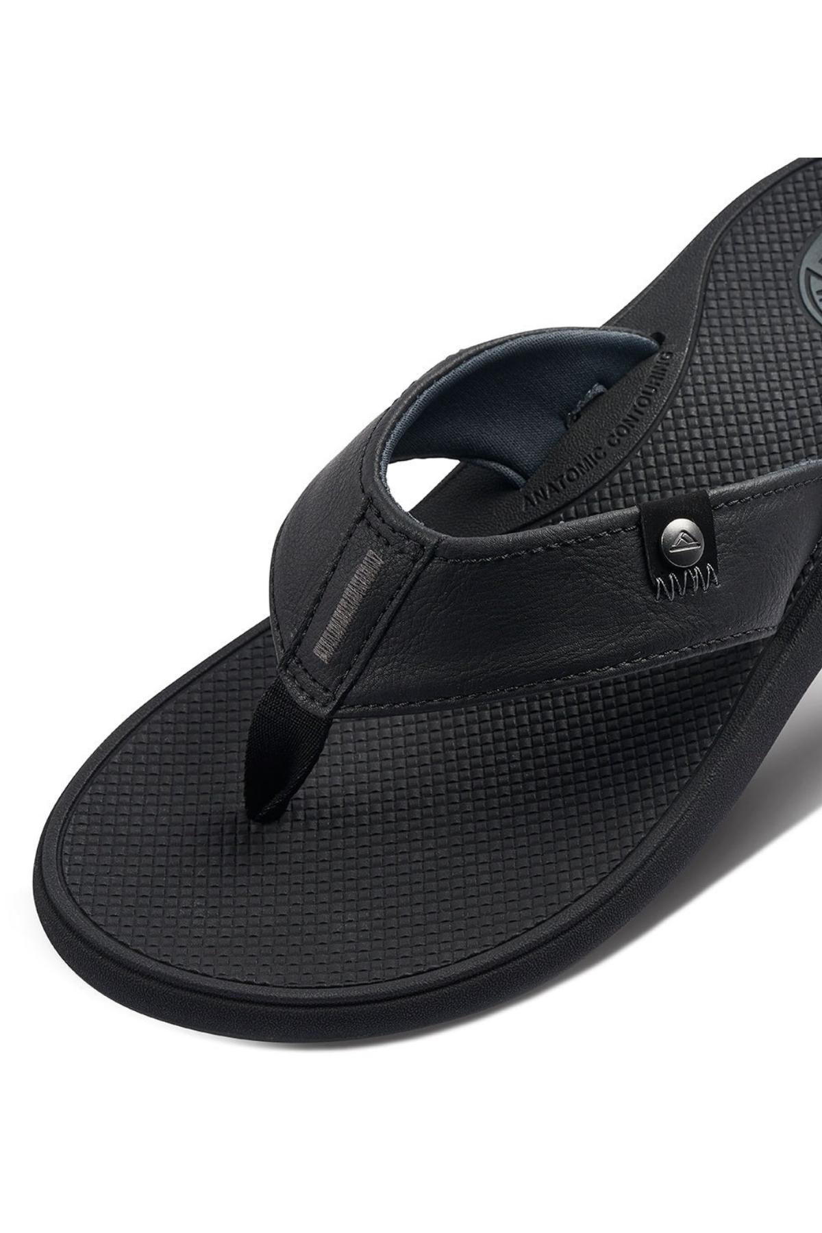 A close-up of the REEF Phantom Nias flip flop sandal in black, showcasing its textured footbed and robust thong strap. The sandal is embellished with metal rivets by the strap and features discreet branding on both the footbed and strap. Designed with longevity in mind, it promises a comfortable fit and durable outsole.