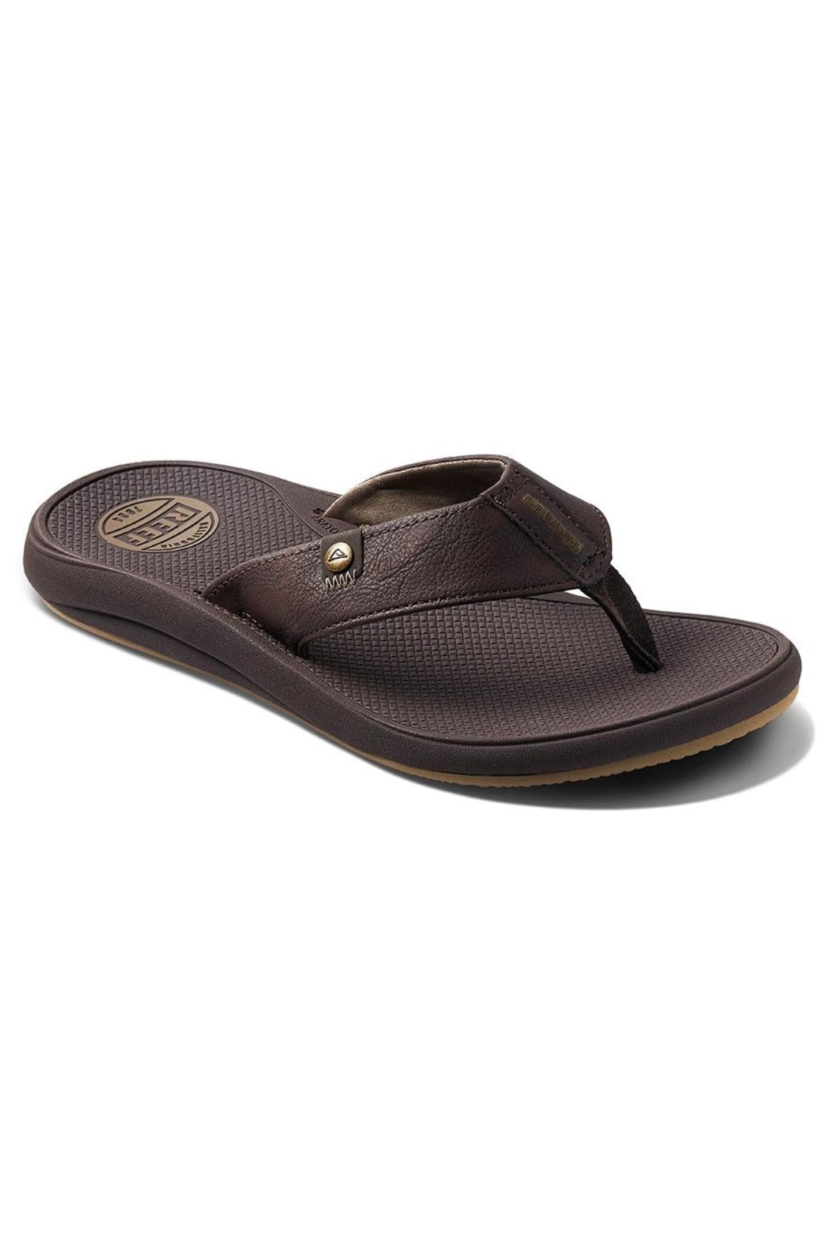 A single REEF Phantom Nias flip-flop sandal, crafted from brown leather, features a textured insole and an emblem on the heel area. It offers superior traction, a wide strap with a small metal detail, and a dark footbed with slight elevation at the heel for enhanced comfort.