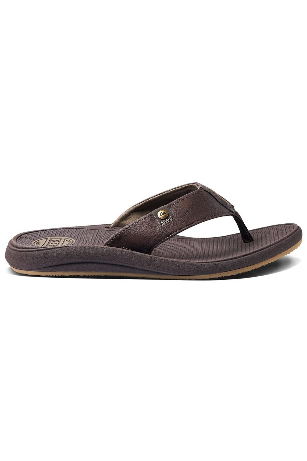 The REEF Phantom Nias flip-flop sandal features a synthetic upper strap adorned with metallic embellishments and a textured sole. The slightly darker brown base has a ribbed footbed and a thin, beige-colored outer edge for contrast. Designed for comfort, it offers superior traction capabilities.