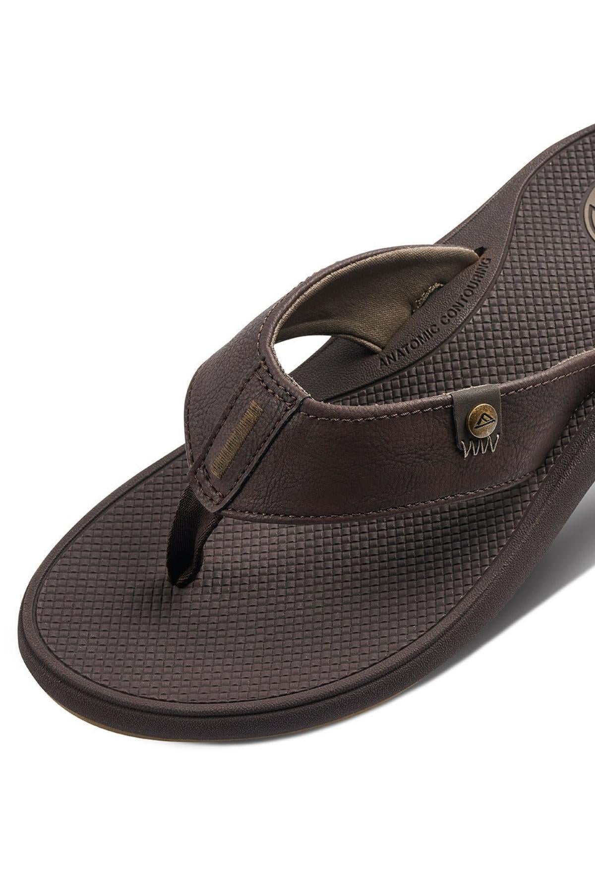 Close-up of the REEF Phantom Nias flip-flop sandal in brown, showcasing its textured footbed and synthetic upper with brand logos and stitching details. This sandal features superior traction capabilities, an ergonomic design, and a toe thong strap for added comfort.