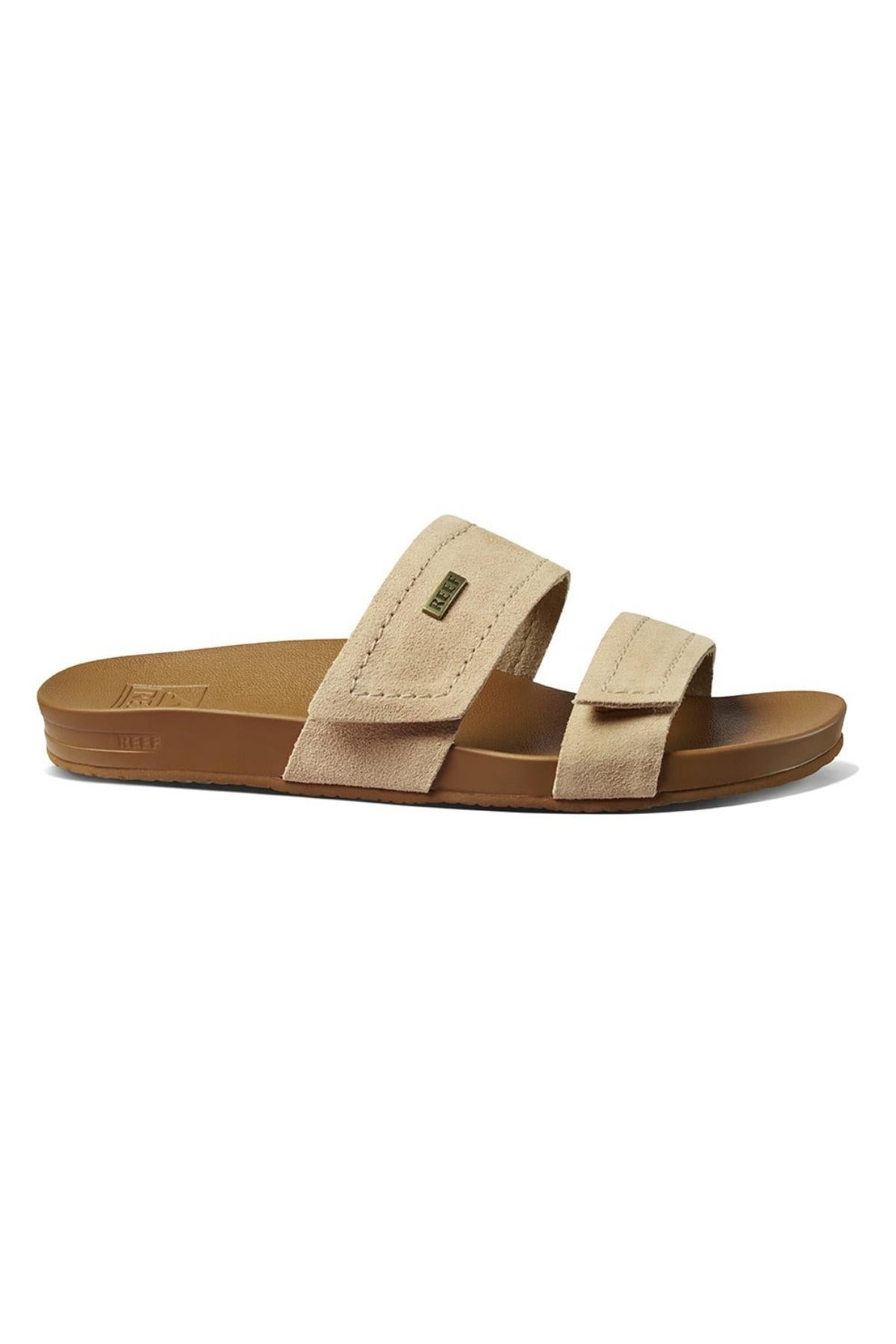 The REEF Velcro Vista SE is a tan sandal with two wide leather straps and a contoured sole. Its minimalist design features soft suede-like material, a cushion bounce midsole for comfort, and a slightly textured sole for grip.