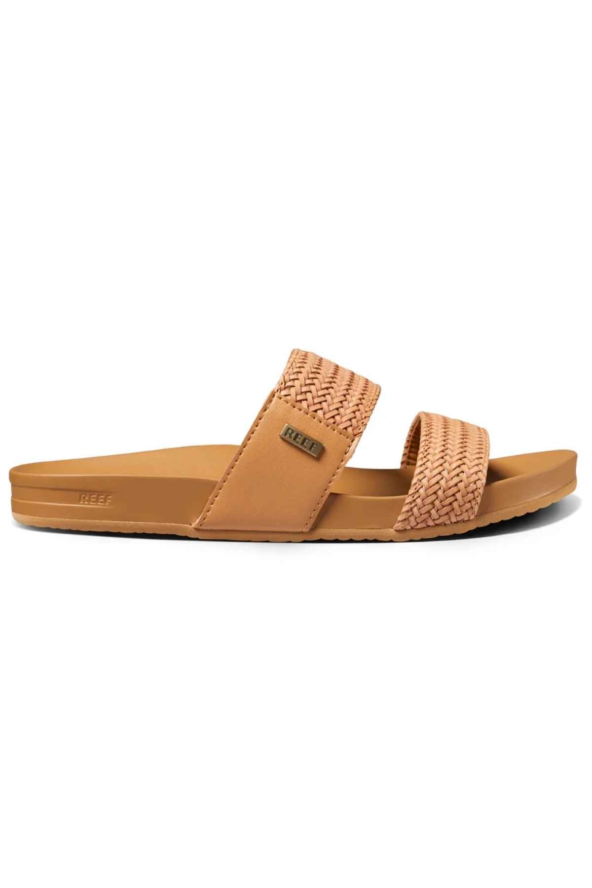 The REEF Vista Braid II sandals have a tan color with one braided and one smooth strap, plus a rectangular tag. They feature a cushioned midsole and slight arch support, making them eco-friendly and ideal for casual outings.