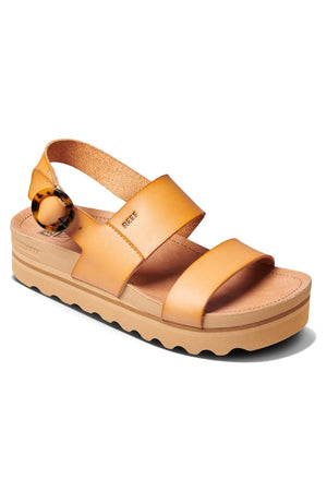 The REEF Vista Hi Buckle sandals are tan, open-toe sandals featuring two wide straps across the foot and a slingback strap with a buckle closure. They come with a vegan leather upper, a platform sole with a ridged bottom for added traction, and arch support for all-day wear.
